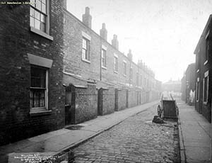Black and white shot of a cobbled Hulme street with fallen cart centre.